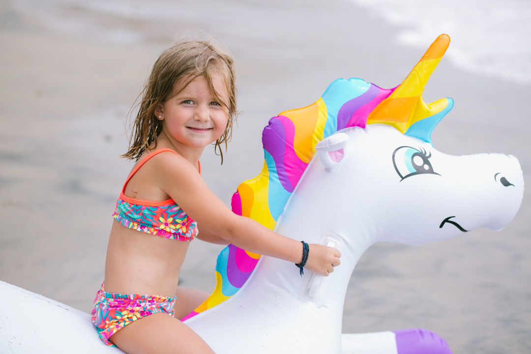 Lisa Allen of LunchPails and Lipstick with her daughters in Solana Beach, CA wearing colorful swimsuits for kids and a unicorn pool float from Kohls